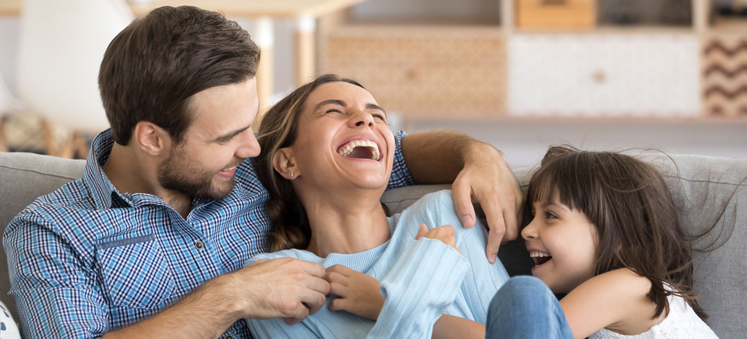 Padre e hija haciendo cosquillas a la madre mientras se ríen sentados en el sofá